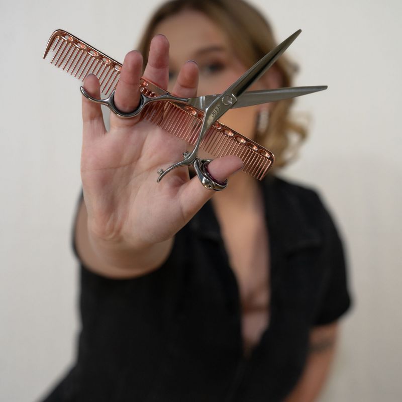 Photo of a cosmetologist holding up haircutting scissors and a comb at Empower Aesthetics Canyon Lake Hair Salon.